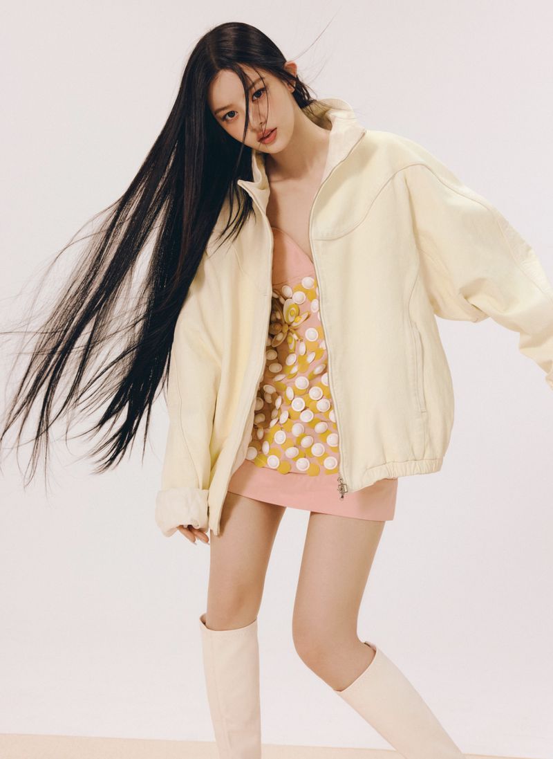 Young woman with long dark hair wearing a cream jacket and pink patterned dress against a white background.