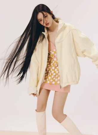 Young woman with long dark hair wearing a cream jacket and pink patterned dress against a white background.