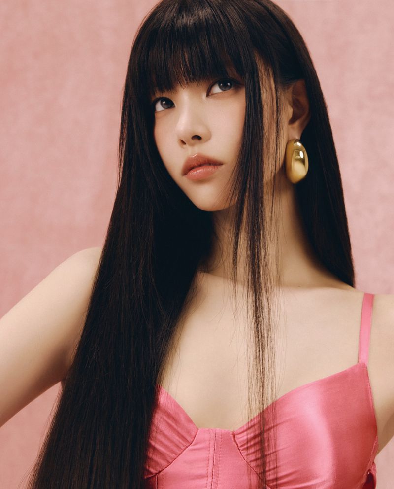 Portrait of young east asian woman with long dark hair wearing pink top and gold earrings against pink background