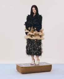 Young woman in a textured black ruffled dress standing on a low cushioned platform against a plain background