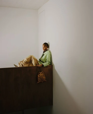Letitia Wright seated against a white wall wearing a light green jacket and voluminous tan trousers for ODDA Magazine