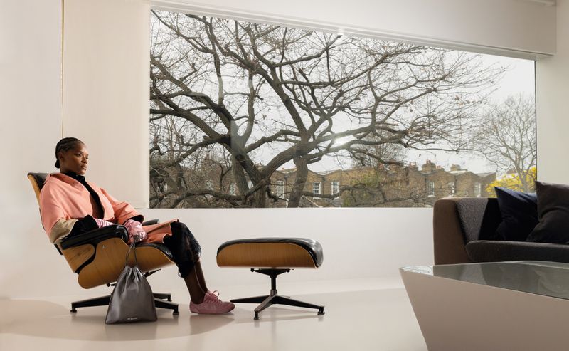 Letitia Wright seated in a modern lounge chair wearing a pink coat against a large window with bare tree views for ODDA Magazine