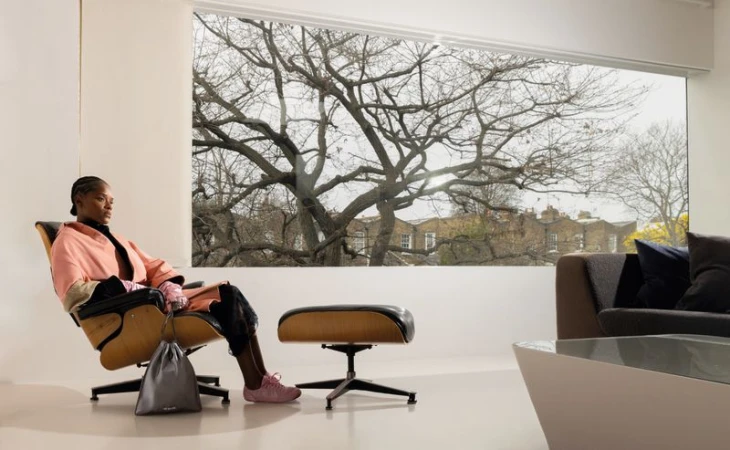 Letitia Wright seated in a modern lounge chair wearing a pink coat against a large window with bare tree views for ODDA Magazine