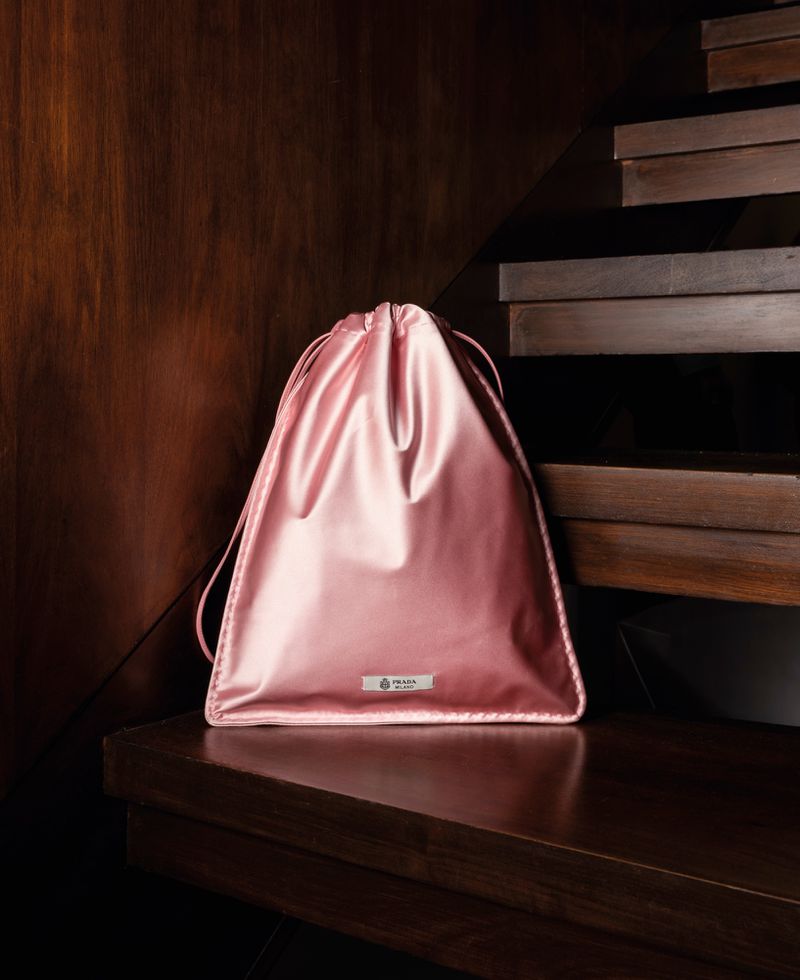 Pink satin drawstring dust bag resting on a dark polished wooden staircase indoors.