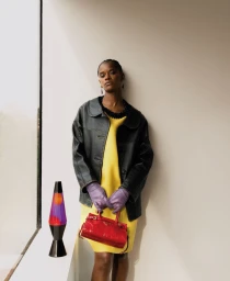 Letitia Wright wearing a yellow dress and black leather jacket holding a red handbag by a lava lamp for ODDA Magazine