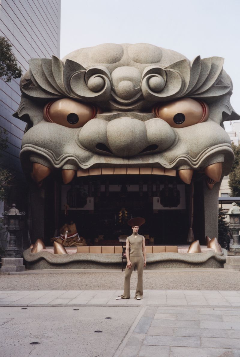 Model wearing neutral toned apparel standing before a large sculpted lion head stage for ODDA Magazine Naniwa Shita no Miya editorial