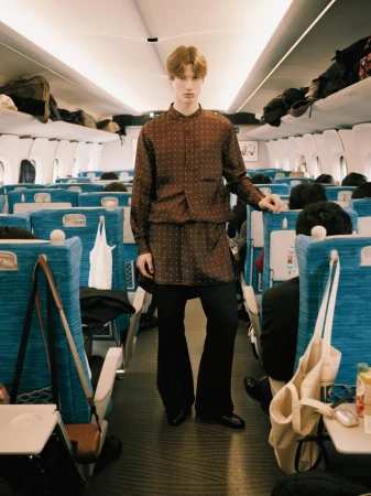 A young male model in a brown patterned shirt standing inside a train carriage for ODDA Magazine