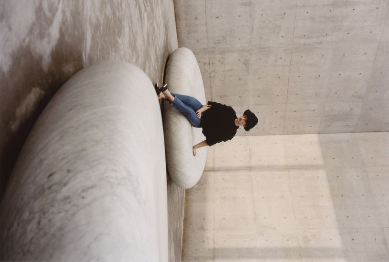 Person seated on a large circular stone structure inside a brutalist concrete room captured by Max Tardio for ODDA Magazine