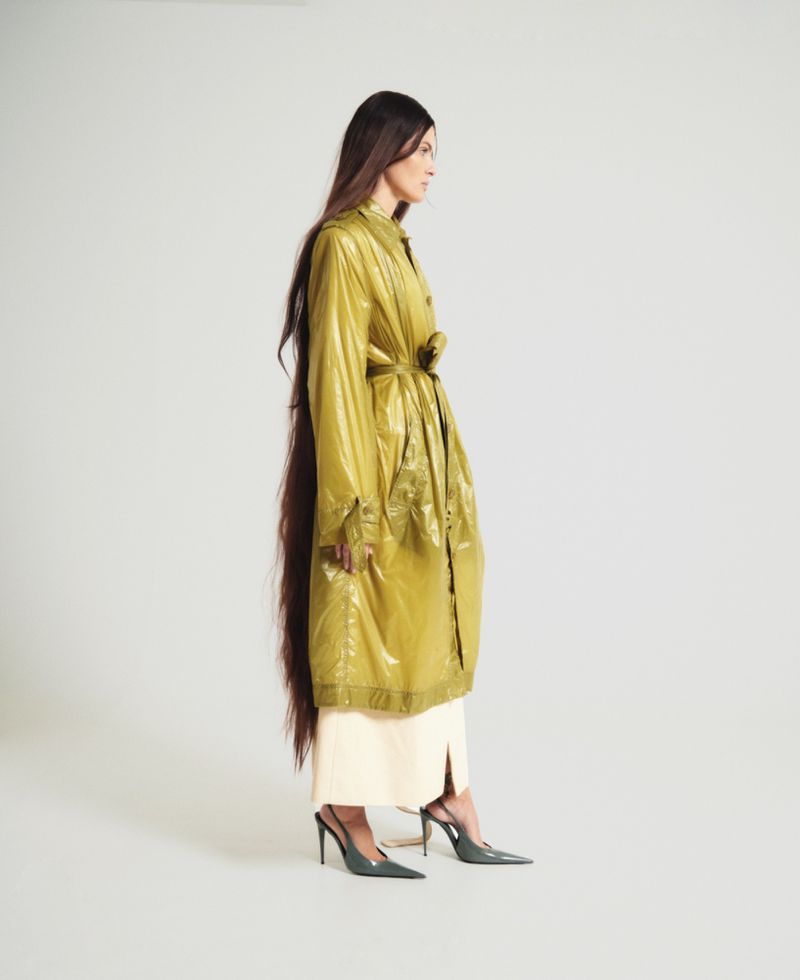 Isabeli Fontana in a shiny olive green coat with very long dark hair against a plain white background for ODDA Magazine.