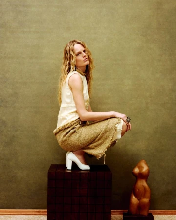 Model Hanne Gaby Odiele crouching on a dark wood block against an olive green textured wall for ODDA Magazine
