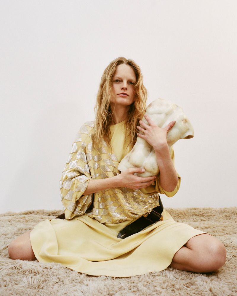 Model Hanne Gaby Odiele holding a sculptural torso object while seated on a textured carpet for ODDA Magazine