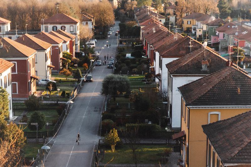 Aerial view of a residential suburban street lined with houses and parked cars under warm sunlight.