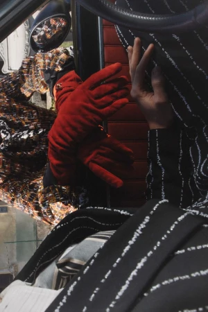Close-up of hands wearing red gloves resting inside a car interior with patterned tweed and striped garments.