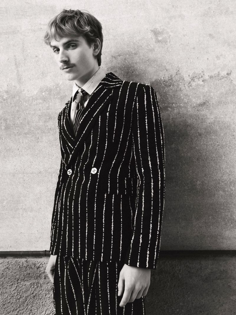 Man wearing a striped double-breasted suit against a textured wall