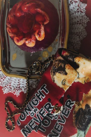 Red patterned handbag with chain strap next to a silver tray holding a circular red molded dish with prawns.
