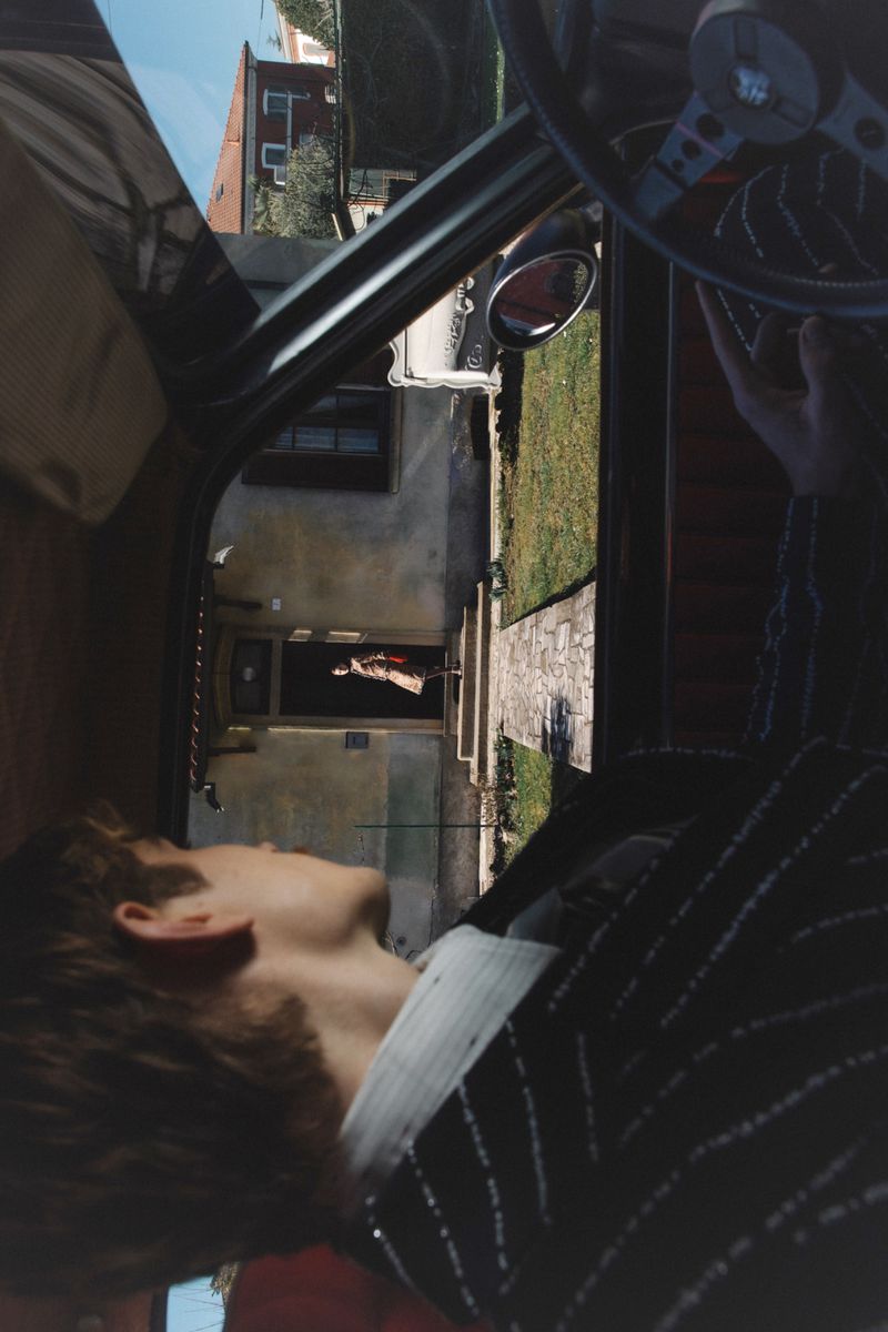 Driver looking through car window at a person standing outside a building for ODDA Magazine project The Uncontrollable Despair