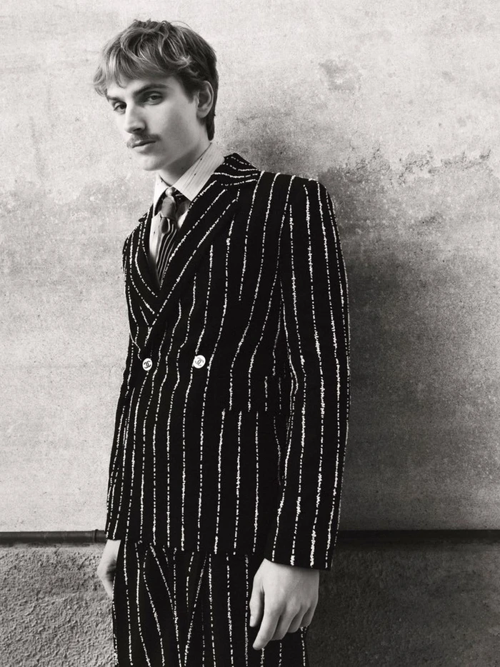 Man wearing a striped double-breasted suit against a textured wall