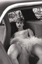 Black and white portrait of a man with a mustache seated inside a car wearing a feather garment.