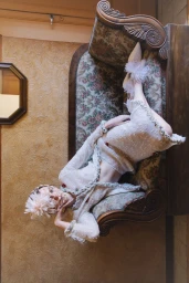 Model lying on an antique patterned sofa wearing an intricate textured white outfit and feathered footwear.
