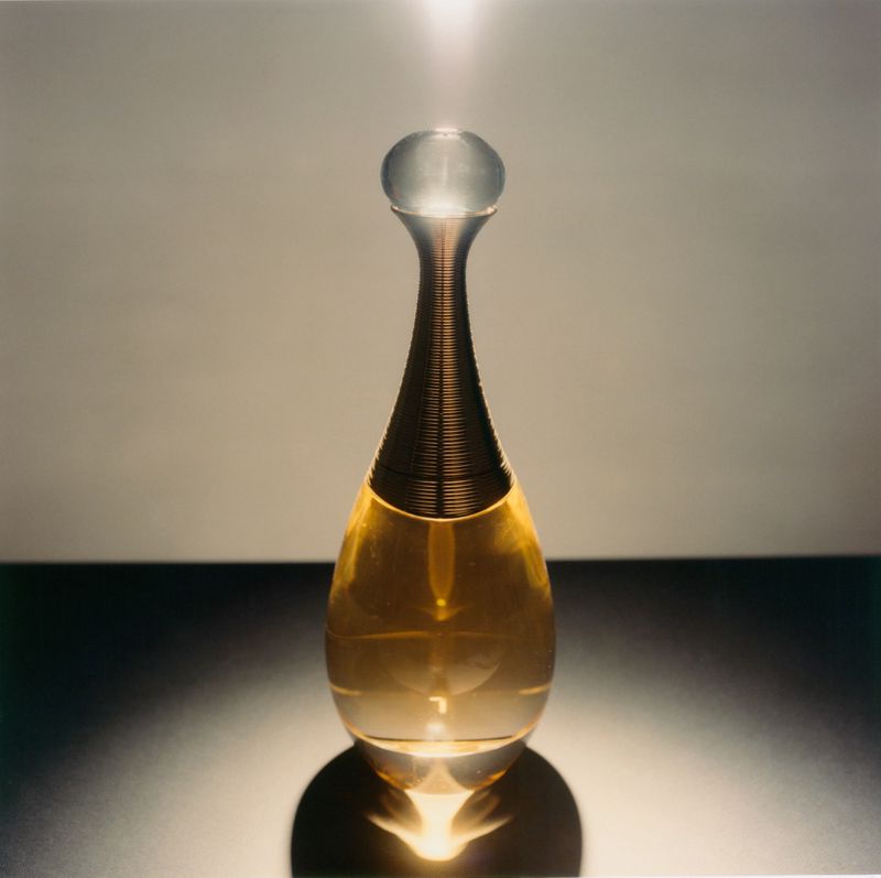 A golden perfume bottle with a rounded cap standing centrally against a minimalist two-tone studio background.