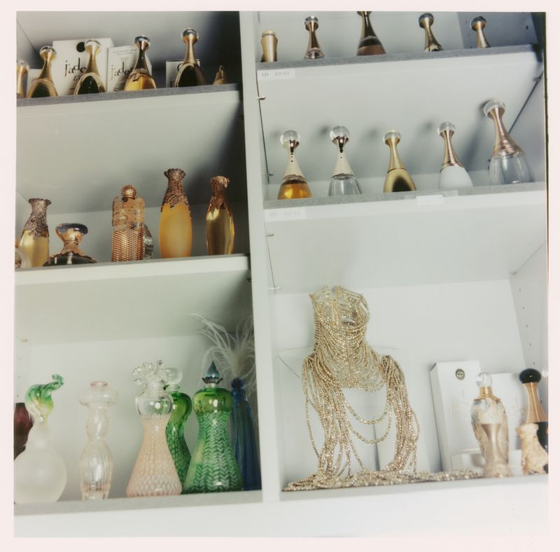 Shelves displaying an assortment of decorative perfume bottles and a beaded necklace in a white display case