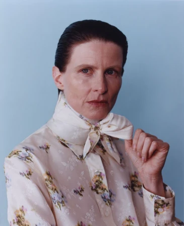 Portrait of a model wearing a patterned cream silk shirt and matching neck scarf against a blue backdrop