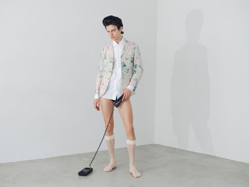 Model in floral blazer and white shirt holding telephone handset against white seamless wall