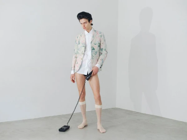 Model in floral blazer and white shirt holding telephone handset against white seamless wall