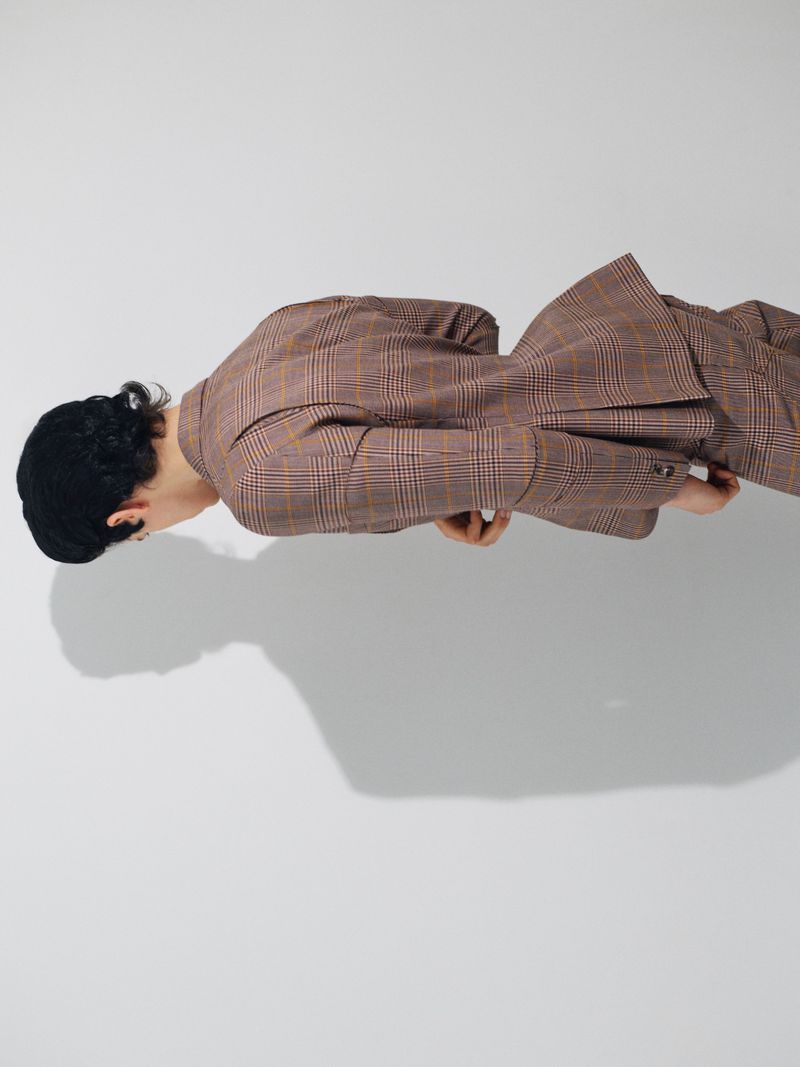 Model wearing a brown plaid suit posed horizontally against a seamless grey background