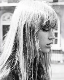 Black and white profile portrait of a woman with textured long hair and bangs looking downward outdoors in natural daylight.