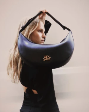 Model holding a curved black leather handbag by the strap in front of a neutral backdrop for ODDA Magazine