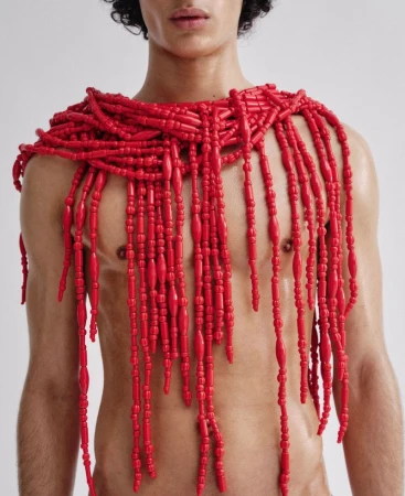 Close-up portrait of a male model wearing an elaborate red beaded necklace draped across his shoulders.