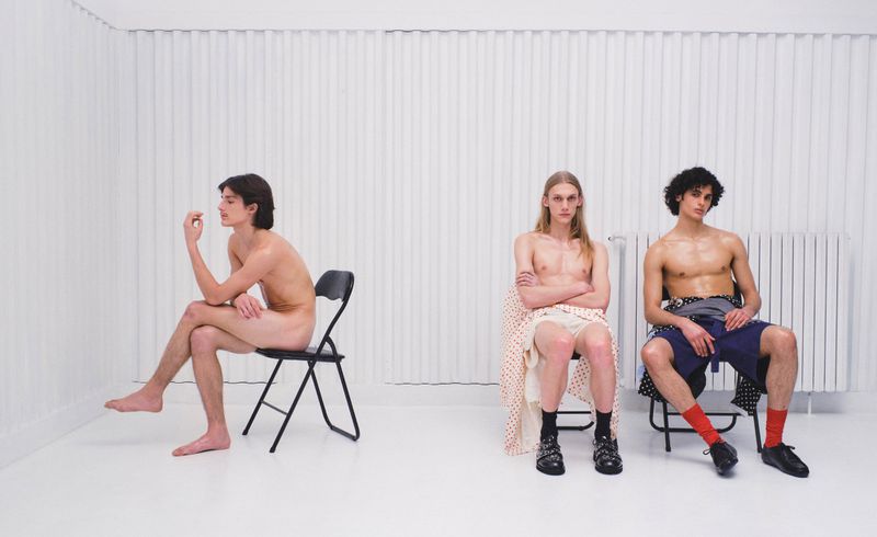 Three male models seated on chairs against a white corrugated wall for an ODDA Magazine fashion editorial.