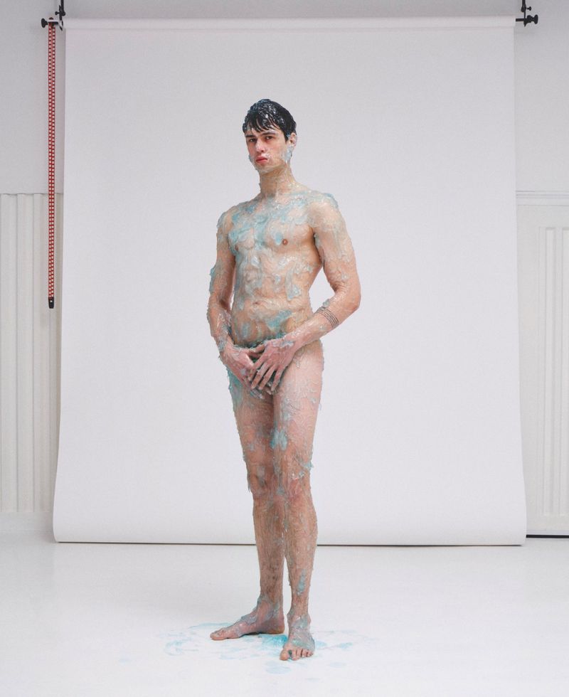 Full-length portrait of a male model covered in blue gel standing against a white seamless backdrop