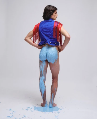 Model from behind wearing a blue vest with red fringe, with blue paint dripping down his legs against a white background