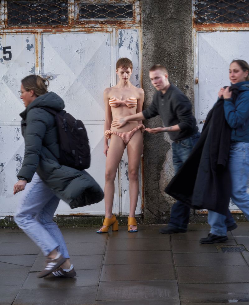 Model wearing striped bikini standing against doors with passersby in an urban street