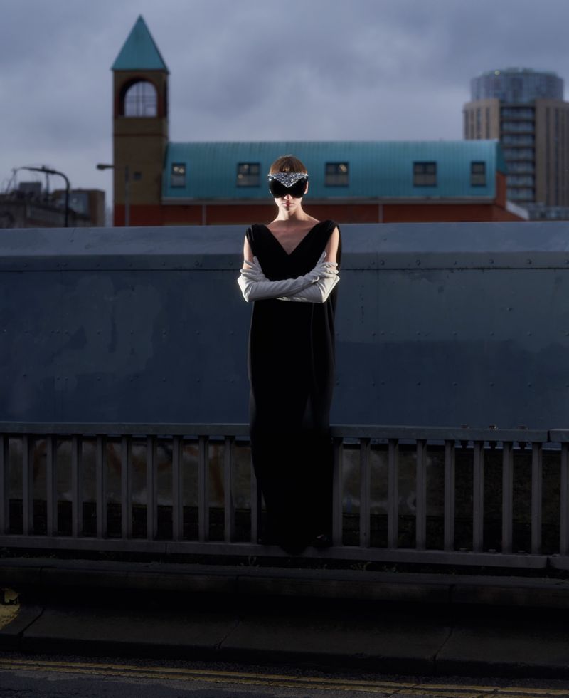 Model in a black dress and white gloves standing on a bridge against a skyline for ODDA Magazine