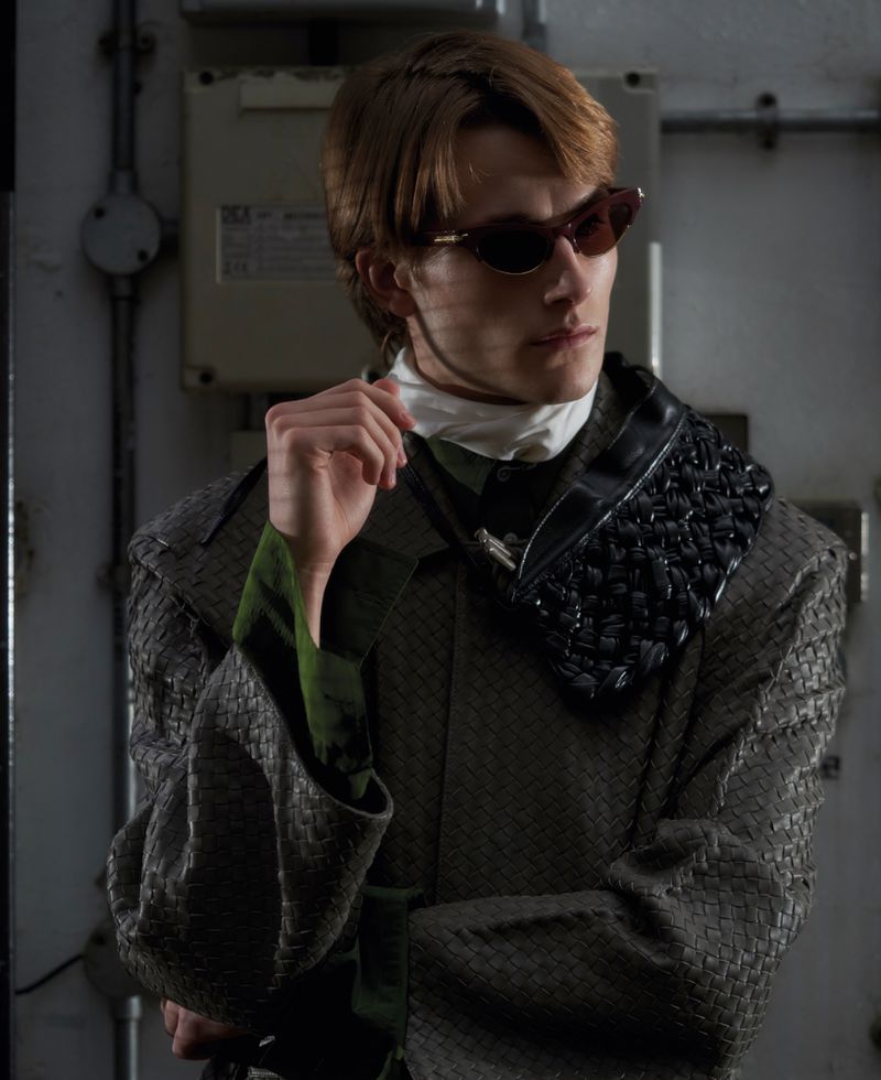 Model wearing dark sunglasses and a textured patterned coat in an industrial setting for ODDA Magazine The Debutants project