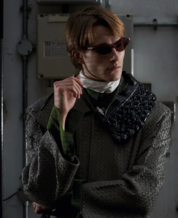 Model wearing dark sunglasses and a textured patterned coat in an industrial setting for ODDA Magazine The Debutants project