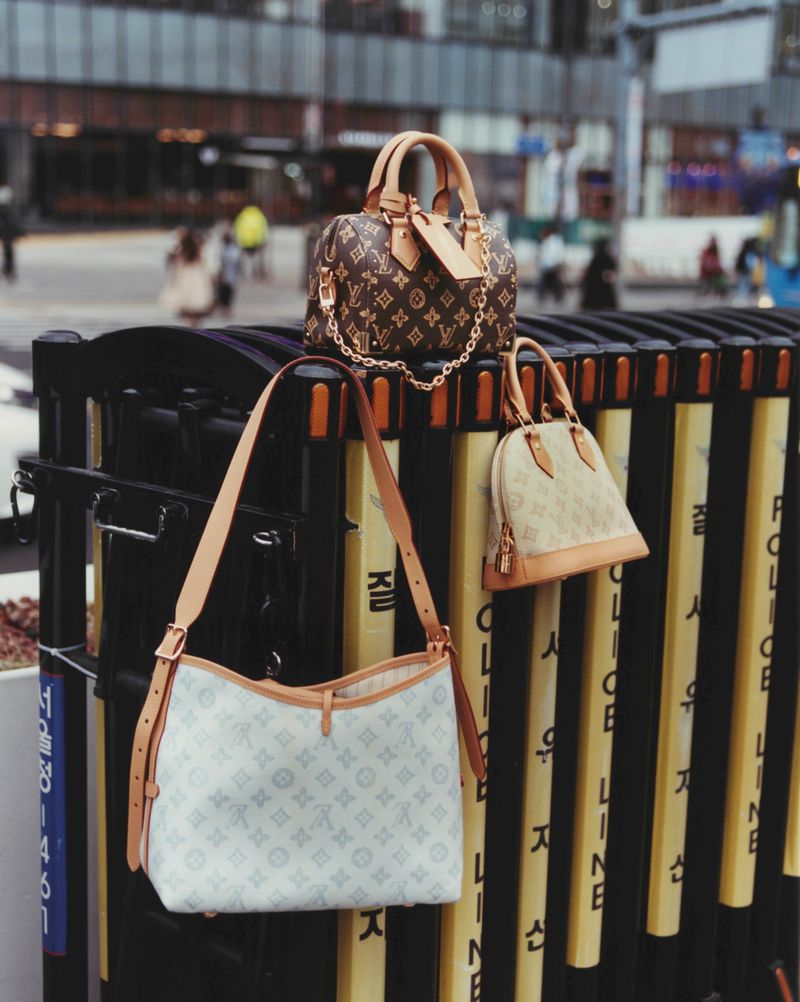 Three designer monogram handbags displayed on a black and yellow street barrier in an urban setting for ODDA Magazine editorial.
