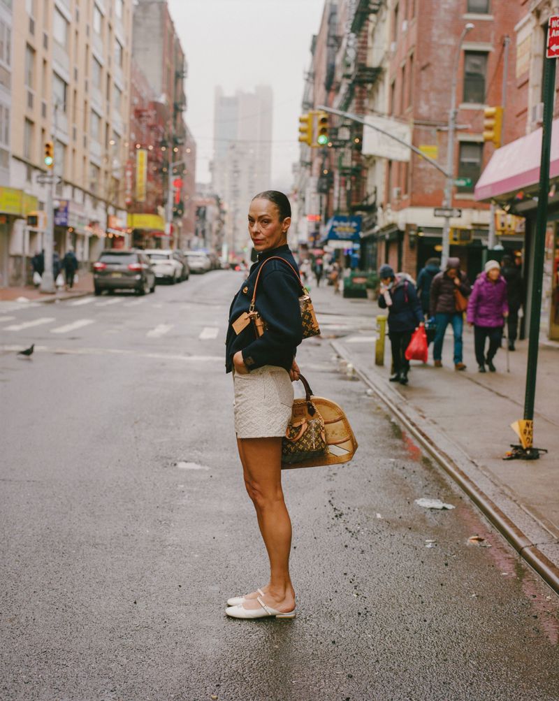Model Carliane Paixao standing on an urban street holding a monogram handbag for ODDA Magazine editorial 1896, and The Rest is History.