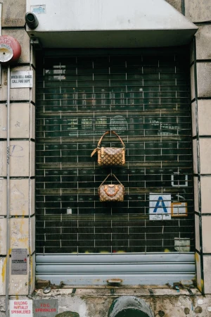 Two monogram handbags hanging on a closed metal security gate of a storefront urban facade