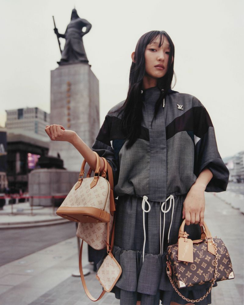 Model Carliane Paixao in a grey jacket holding monogram handbags in a public square for ODDA Magazine