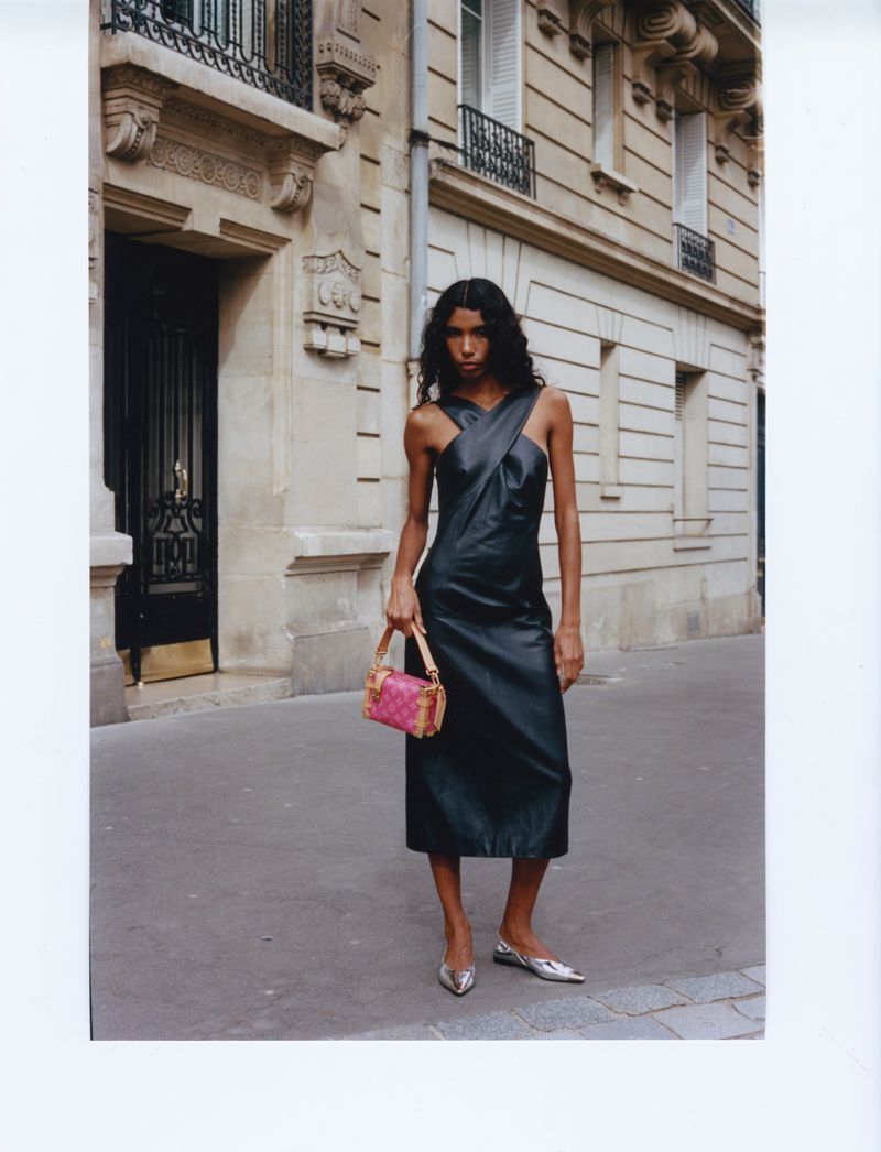 Model Carliane Paixao wearing a black leather dress and holding a pink handbag on a Parisian street for ODDA Magazine.