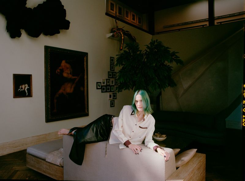 Model with dyed teal hair reclining on a modern couch in a residential interior for ODDA Magazine