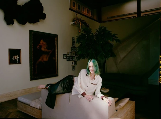 Model with dyed teal hair reclining on a modern couch in a residential interior for ODDA Magazine