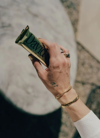 Close-up of a person holding a protein bar, wearing gold bracelets and rings