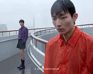 Two male models on a rooftop in the rain, one in a red jacket in the foreground and one in purple standing behind