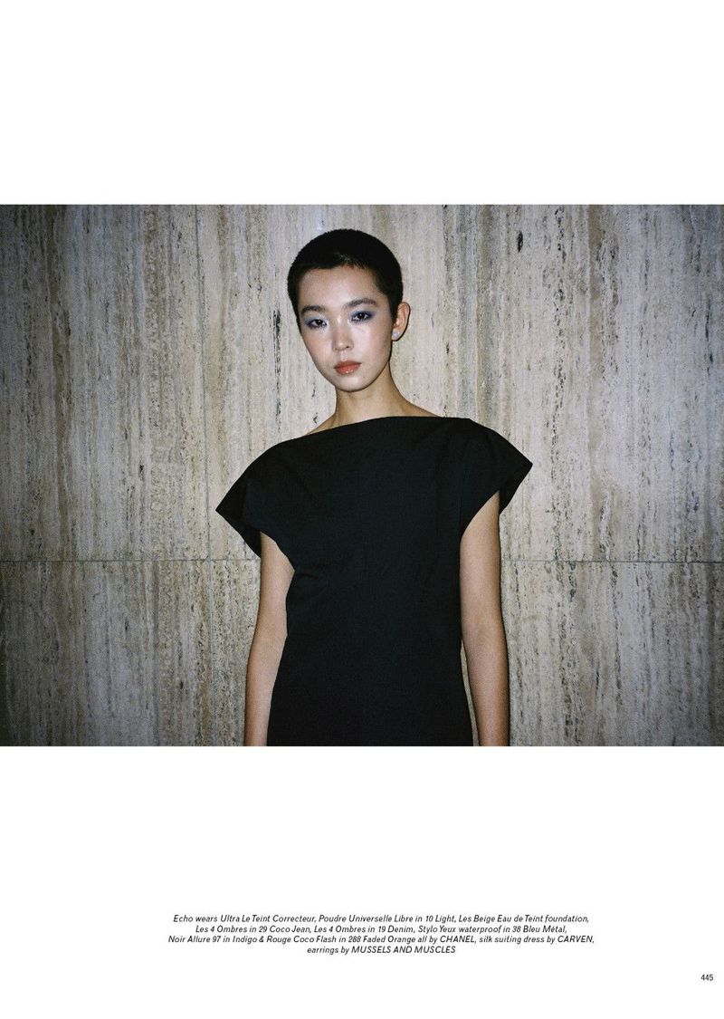 Model with short hair wearing a black dress against a textured stone wall background