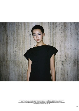 Model with short hair wearing a black dress against a textured stone wall background